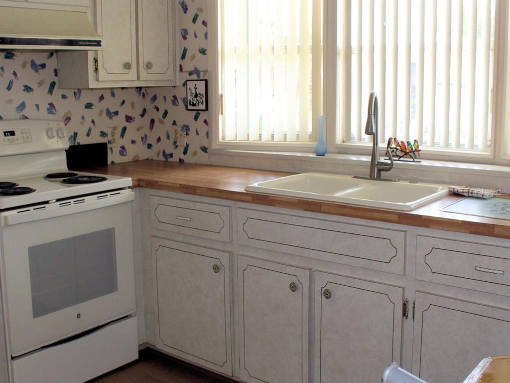 A kitchen features white cabinets, a wood countertop, a white stove, and patterned wallpaper — 802 DATE PALM STREET, LARGO, FL