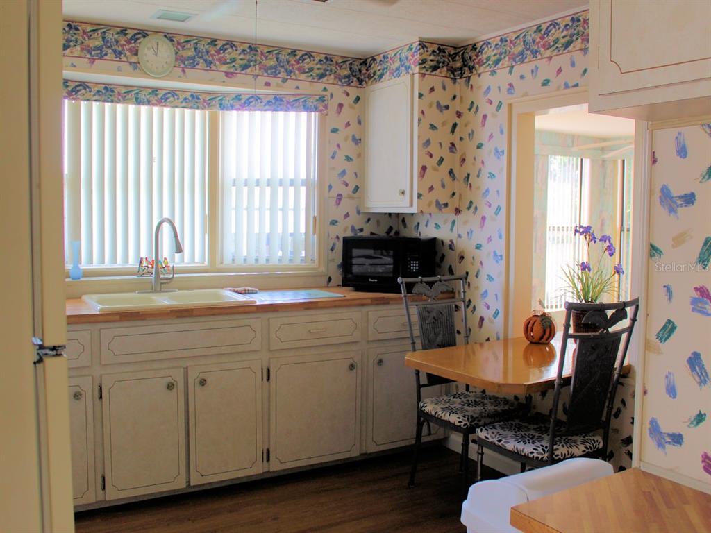 A kitchen features white cabinets, a wood countertop, patterned wallpaper, and a small dining area — 802 DATE PALM STREET, LARGO, FL