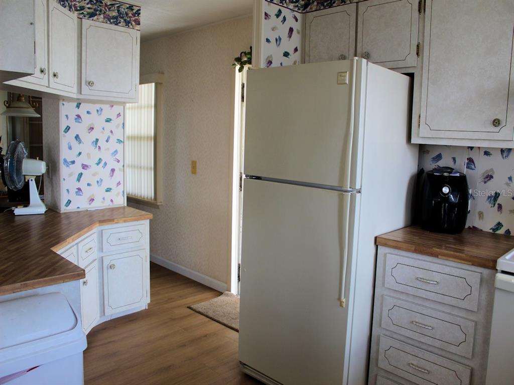 A kitchen features white cabinets, wood-look countertops, a white refrigerator, and patterned wallpaper — 802 DATE PALM STREET, LARGO, FL