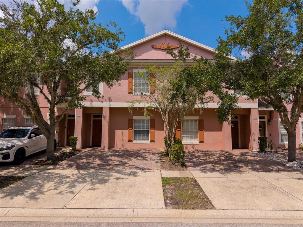 A two-story pink townhouse with a paved driveway and two front entrances — 2328 CARAVELLE CIRCLE, KISSIMMEE, FL