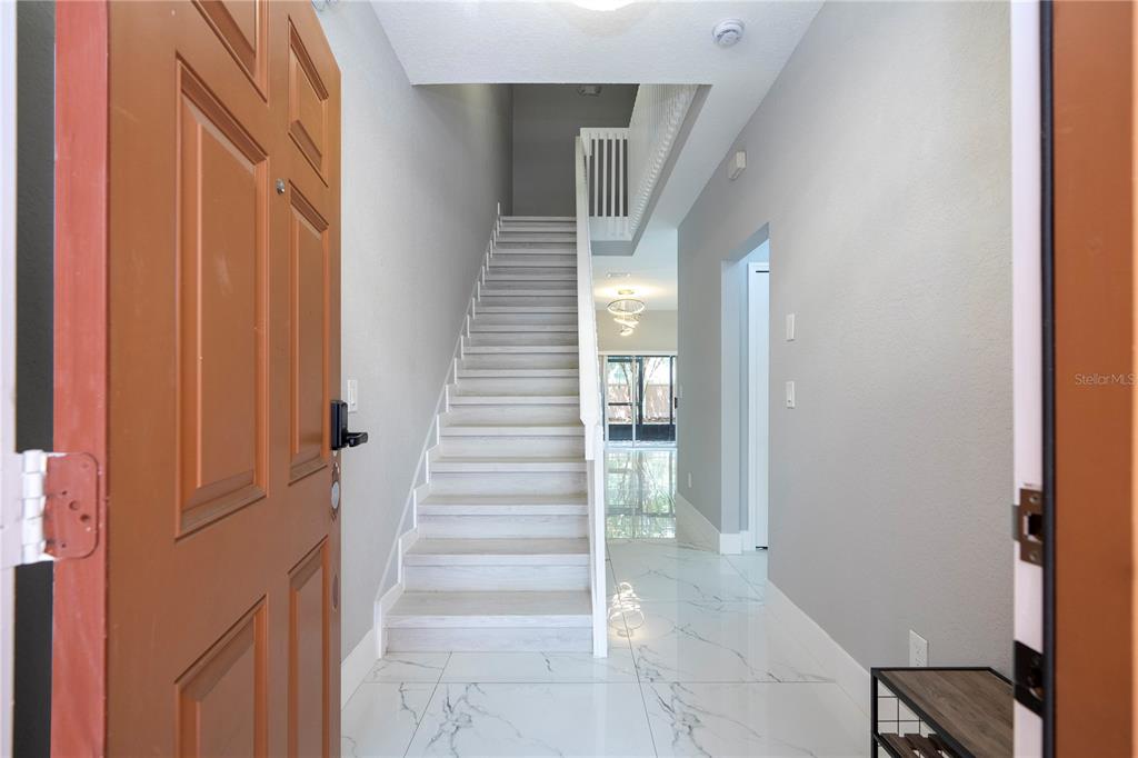 An entryway features a staircase with light wood treads, white tile flooring, and gray walls — 2328 CARAVELLE CIRCLE, KISSIMMEE, FL
