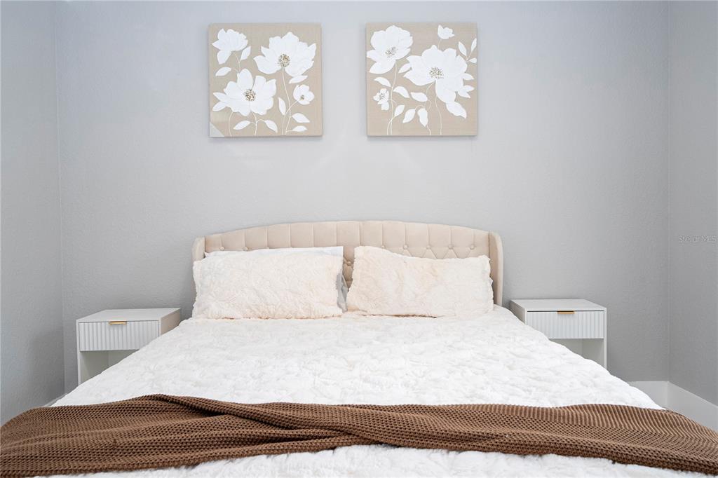A bedroom features a tufted headboard, white bedding, two nightstands, and floral wall art — 2328 CARAVELLE CIRCLE, KISSIMMEE, FL