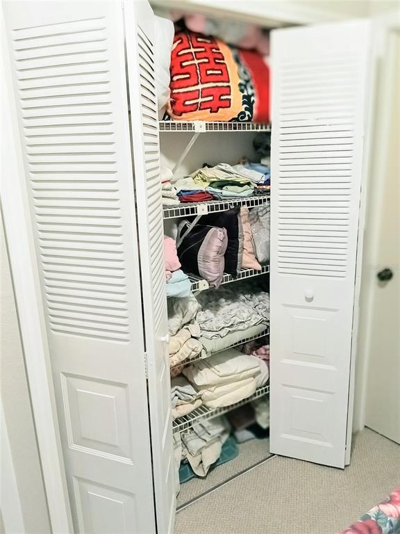 A white louvered-door closet features wire shelving filled with folded linens and pillows — 6640 121ST AVENUE UNIT 1, LARGO, FL