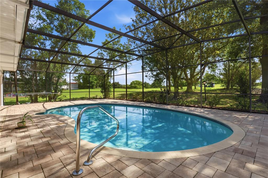 A screened-in patio features a kidney-shaped swimming pool surrounded by light-colored stone pavers — 2249 E UNION CIRCLE, DELTONA, FL