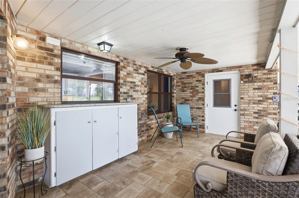 A covered brick patio features a ceiling fan, white storage cabinets, and outdoor seating — 2249 E UNION CIRCLE, DELTONA, FL