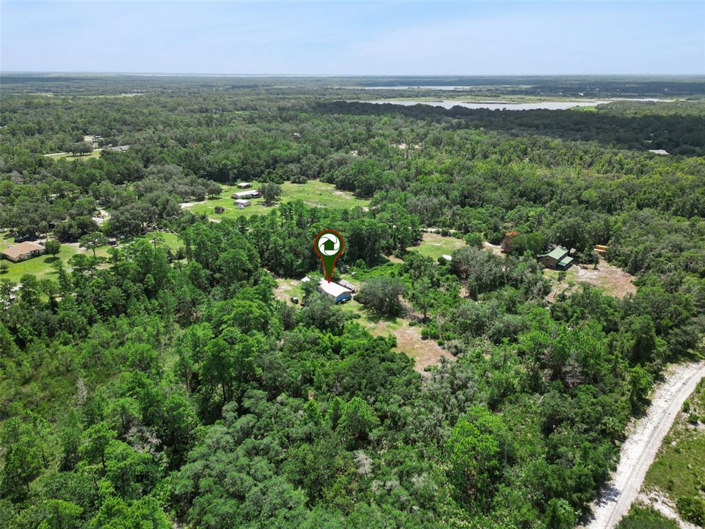 An aerial view shows a house surrounded by dense trees and a dirt road — 680 WILD ACRES ROAD, OSTEEN, FL