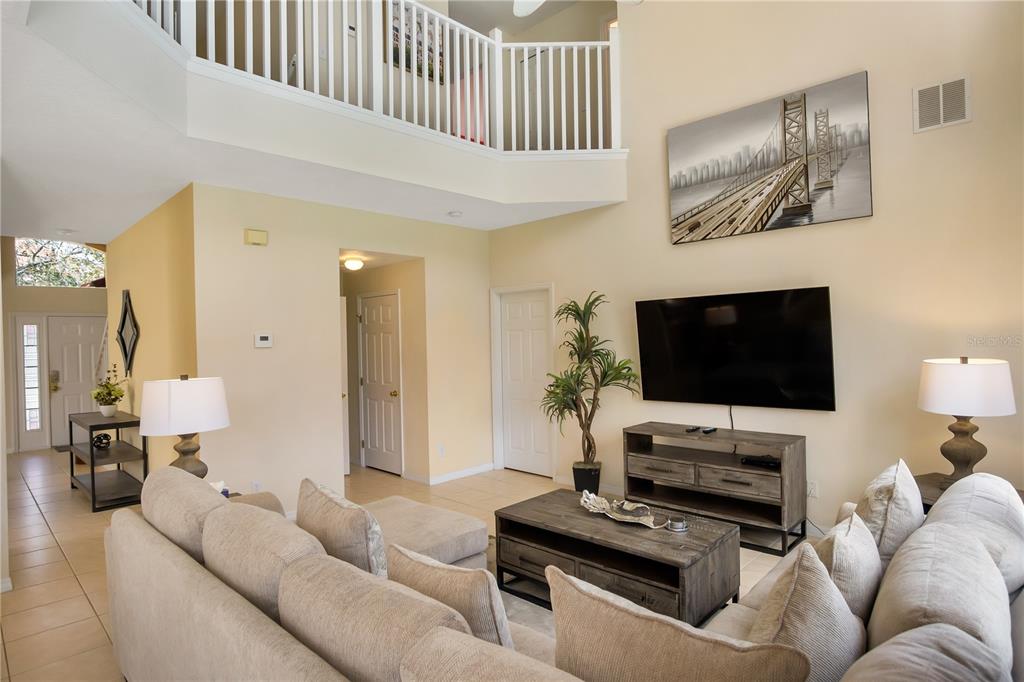 A living room features a sectional sofa, a television, and a balcony overlooking the space — 134 SEVILLA AVENUE, DAVENPORT, FL