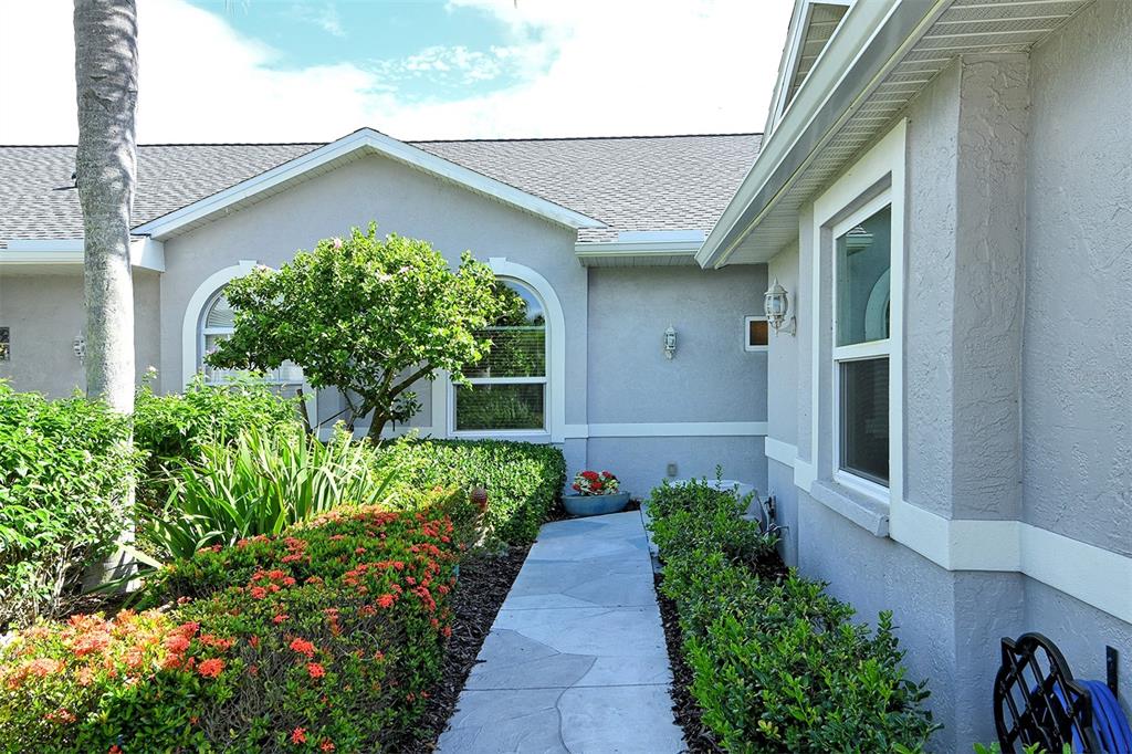 A stone walkway leads to the entrance of a gray house with arched windows and landscaping — 4951 CHASE OAKS DRIVE, SARASOTA, FL