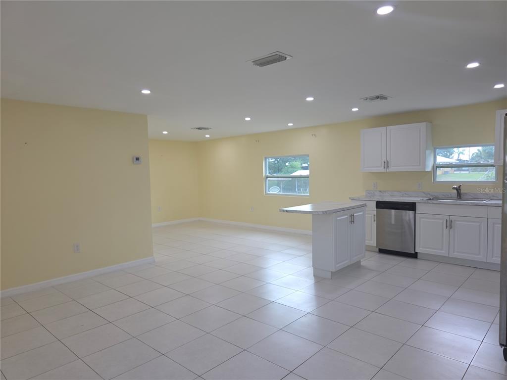 An open-concept kitchen and living area features yellow walls, white cabinets, and tiled floors — 3633 SE 20TH TERRACE, OKEECHOBEE, FL