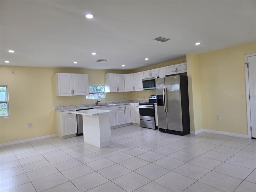A kitchen with white cabinets, stainless steel appliances, a small island, and light-colored tile flooring — 3633 SE 20TH TERRACE, OKEECHOBEE, FL