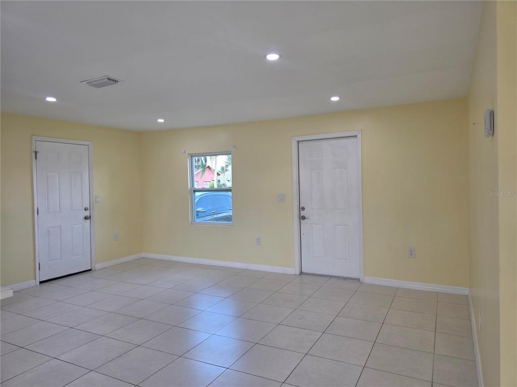 An empty room with light yellow walls, tile flooring, two white doors, and a window — 3633 SE 20TH TERRACE, OKEECHOBEE, FL