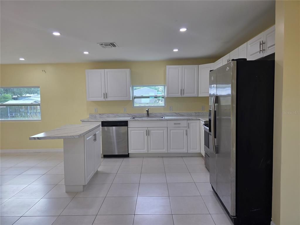 A kitchen features white cabinets, stainless steel appliances, a marble-look countertop, and light-colored tile flooring — 3633 SE 20TH TERRACE, OKEECHOBEE, FL