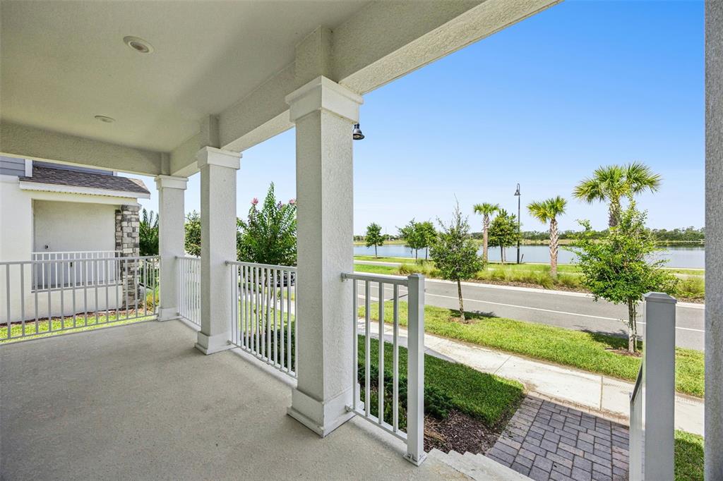 A covered porch with white railings overlooks a street, green lawn, and a lake — 2975 ADDISON BOULEVARD, ST CLOUD, FL