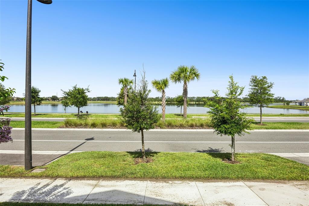A view of a street with young trees, a grassy median, and a lake beyond — 2975 ADDISON BOULEVARD, ST CLOUD, FL