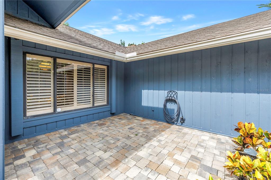A paved patio area sits in the corner of a house with blue vertical siding — 2837 SABER DRIVE, CLEARWATER, FL