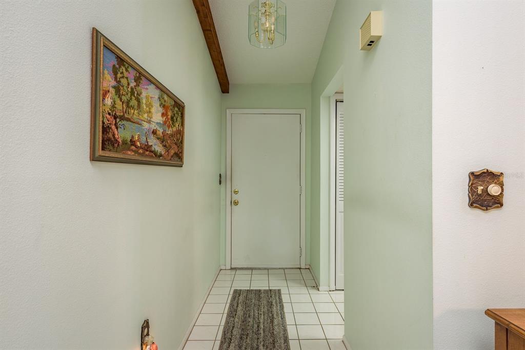 A tiled entryway features a white front door, a wooden ceiling beam, and wall art — 9910 EAGLES POINT CIRCLE UNIT 3, PORT RICHEY, FL