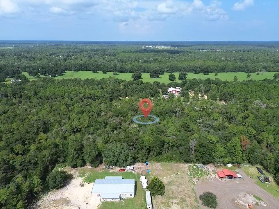 An aerial view shows a wooded lot with a red-roofed house in the distance — TBD NE 135TH TERRACE, WILLISTON, FL