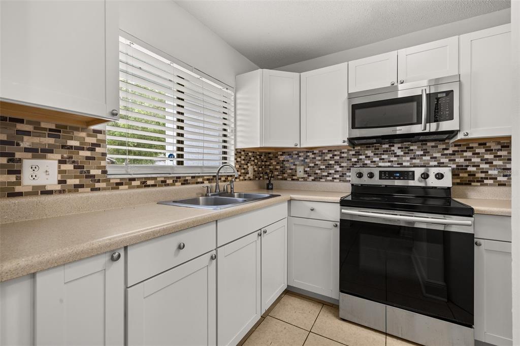 A kitchen features white cabinets, a stainless steel stove, and a mosaic tile backsplash — 111 MICHELLE LANE UNIT B, KISSIMMEE, FL