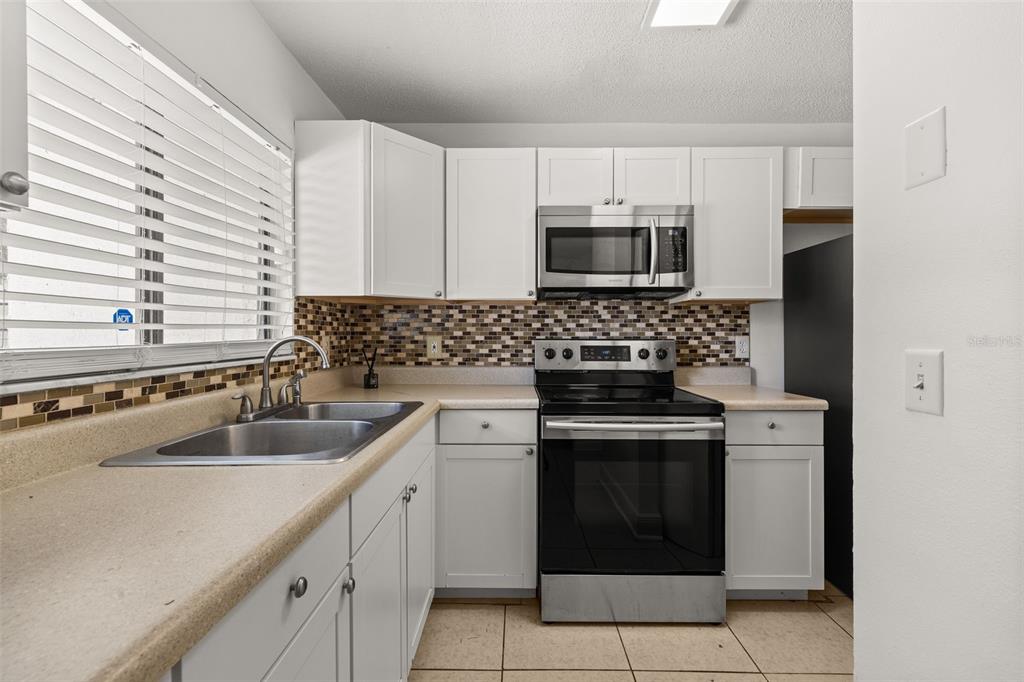 A kitchen with white cabinets and stainless steel appliances opens to a tiled living area — 111 MICHELLE LANE UNIT B, KISSIMMEE, FL