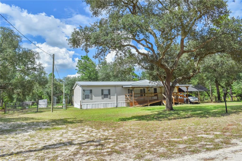 A single-story mobile home with a wooden porch sits on a grassy lot under trees — 10851 NE 76TH STREET, BRONSON, FL