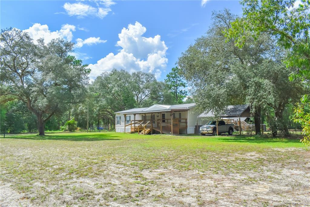 A single-story manufactured home with a wooden porch and carport sits on a grassy lot — 10851 NE 76TH STREET, BRONSON, FL