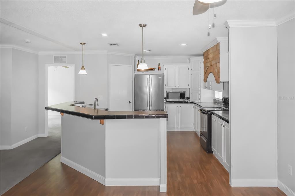 A kitchen with white cabinets, stainless steel appliances, and a tiled breakfast bar countertop — 10851 NE 76TH STREET, BRONSON, FL