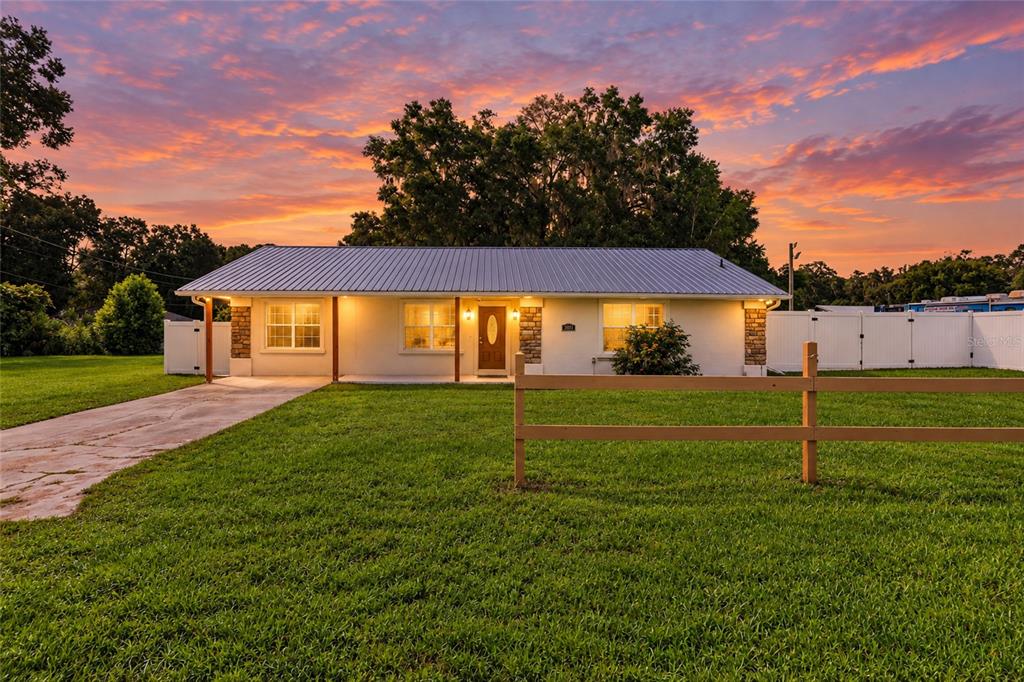A single-story house with a metal roof and a wooden fence at sunset — 3420 SE 135TH LANE, SUMMERFIELD, FL