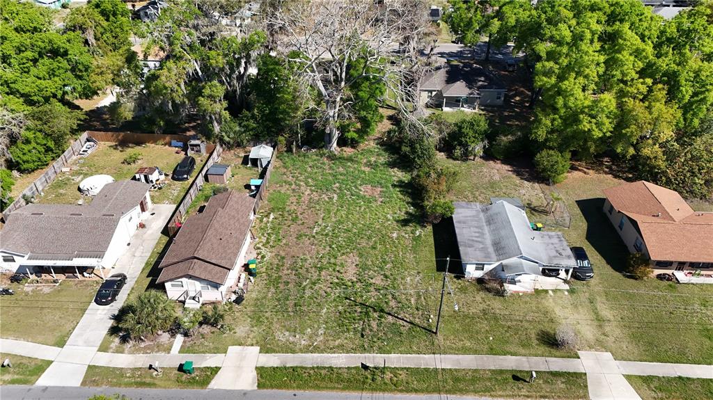An aerial view shows a vacant lot situated between two residential houses on a street — E HAZZARD, EUSTIS, FL