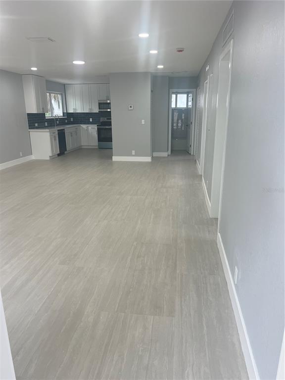 A kitchen with white cabinets and gray tile flooring opens into a spacious living area — 836 SW 2ND TERRACE, DEERFIELD BEACH, FL