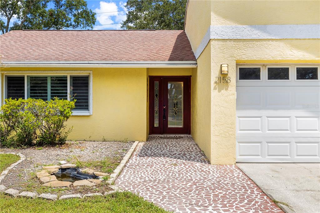 A yellow house exterior features a red front door, a garage, and a stone walkway — 2158 KARAN WAY, CLEARWATER, FL