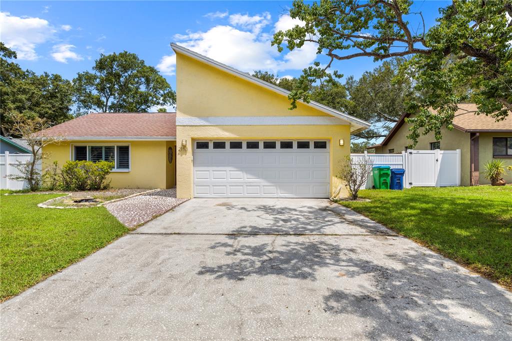 A yellow single-story house features a prominent slanted roofline and a two-car garage — 2158 KARAN WAY, CLEARWATER, FL