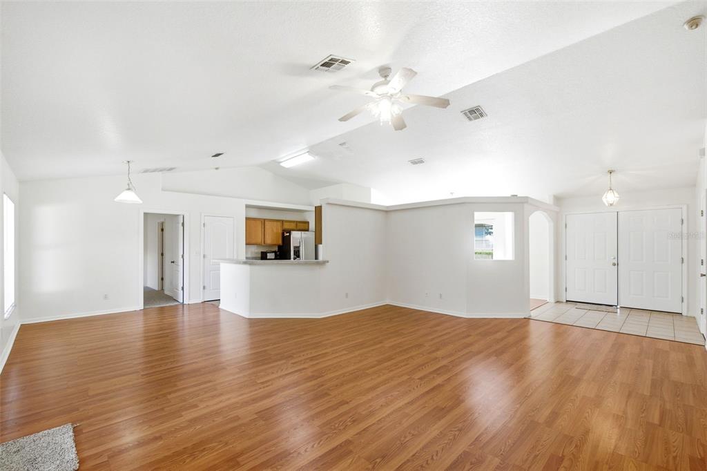 A spacious living area features wood-look flooring, vaulted ceilings, and an open kitchen with counters — 10320 VISTA PINES LOOP, CLERMONT, FL