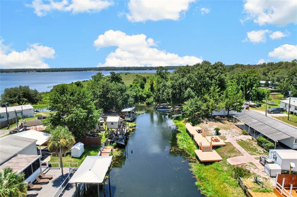 An aerial view shows a narrow canal leading to a lake, flanked by houses and docks — 13651 NE 237TH COURT, FORT MC COY, FL