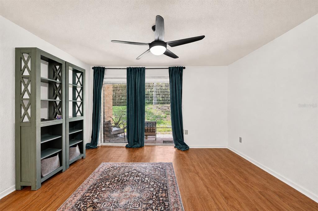 A room with wood-look flooring, a ceiling fan, a bookshelf, and sliding glass doors — 1810 NW 23RD BOULEVARD UNIT 230A, GAINESVILLE, FL