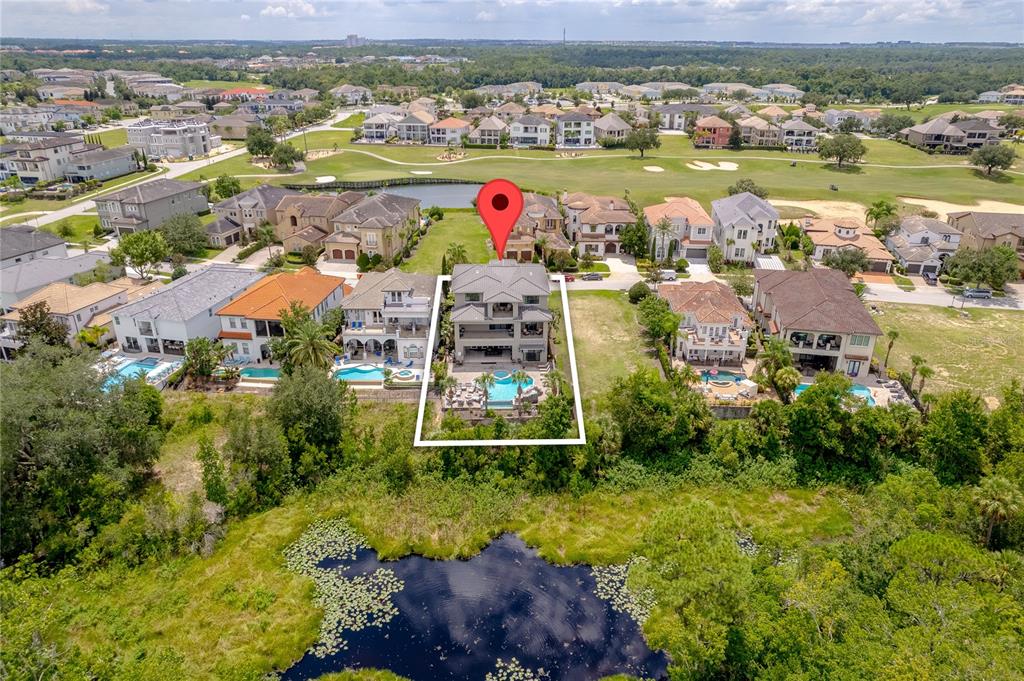 An aerial view shows a multi-story house with a pool overlooking a pond and golf course — 600 MUIRFIELD LOOP, REUNION, FL