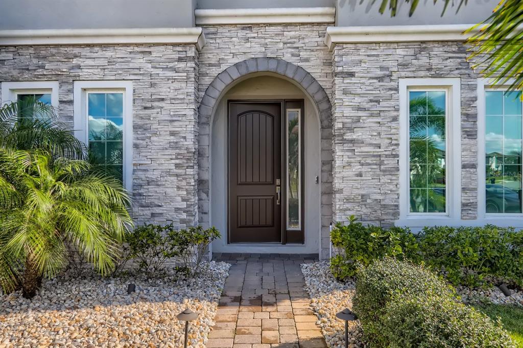 A stone-veneer house exterior features an arched entryway with a dark wood front door — 8192 LUDINGTON CIRCLE, ORLANDO, FL