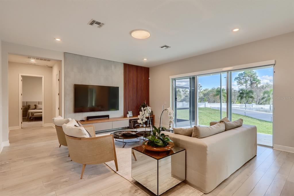 A modern living room features a concrete and wood-slat accent wall, television, and sliding glass doors — 8192 LUDINGTON CIRCLE, ORLANDO, FL