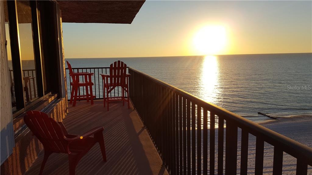 A balcony with red chairs overlooks the ocean during a sunset — 15316 GULF BOULEVARD UNIT 604, MADEIRA BEACH, FL