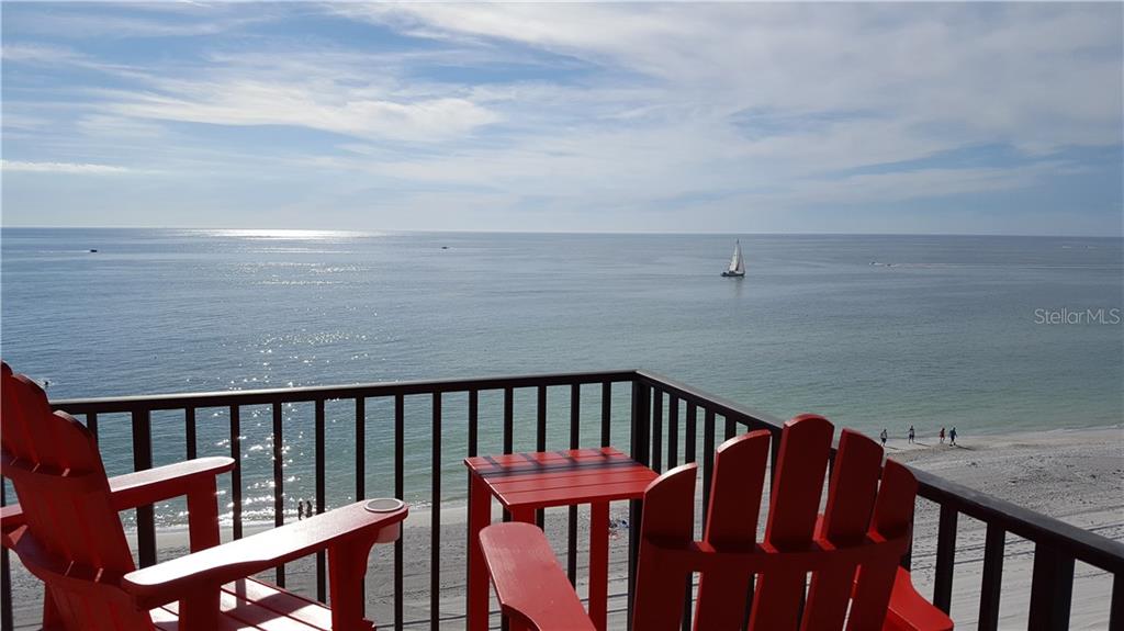 A balcony with two red Adirondack chairs and a small table overlooks the ocean — 15316 GULF BOULEVARD UNIT 604, MADEIRA BEACH, FL