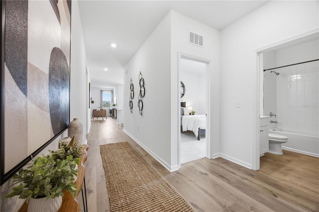 A hallway with light wood floors leads to a bedroom and a bathroom with a tub — 5731 HIAWASSEE ROAD, LEESBURG, FL
