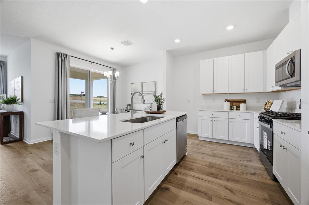 A modern kitchen features white cabinetry, a central island with a sink, and wood-look flooring — 5731 HIAWASSEE ROAD, LEESBURG, FL