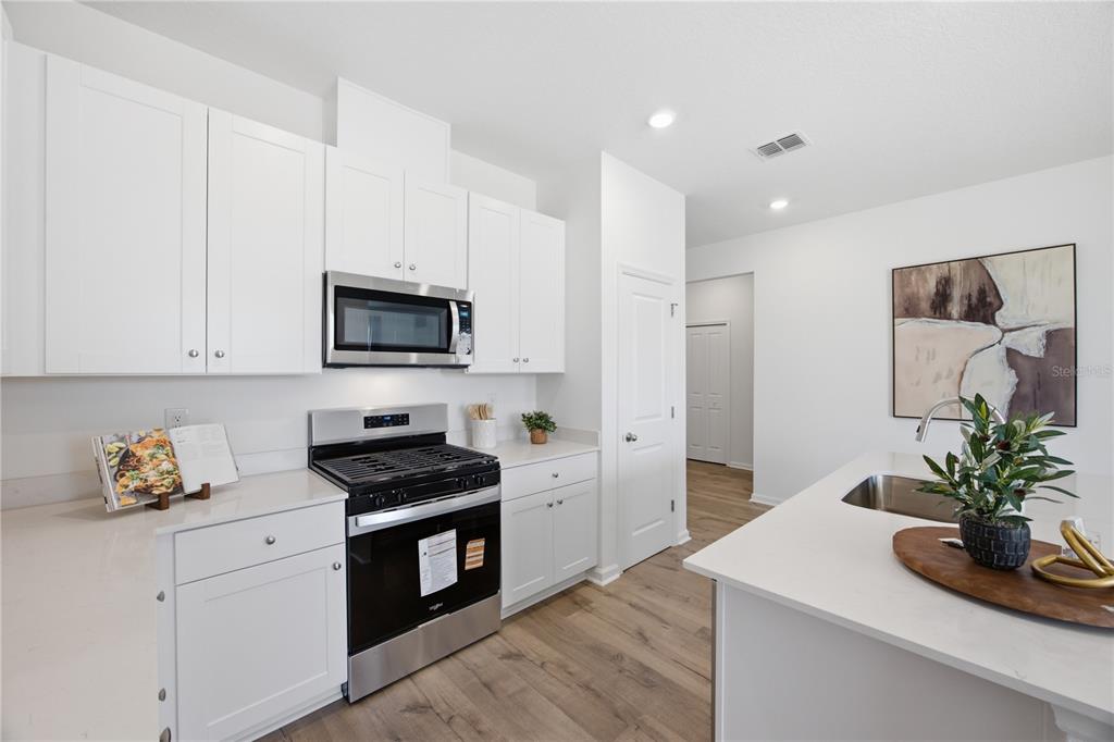 A modern kitchen features white cabinets, stainless steel appliances, and a white quartz island — 5731 HIAWASSEE ROAD, LEESBURG, FL