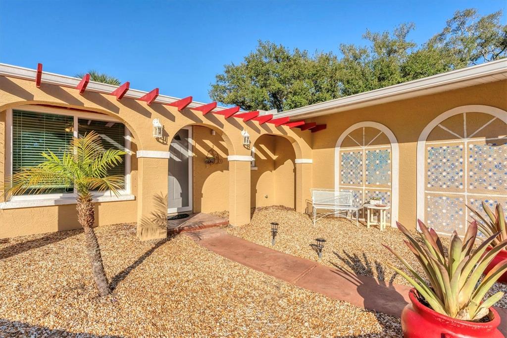 A tan house exterior features a red pergola, a gravel yard, and arched decorative windows — 2745 ARROWHEAD ROAD, VENICE, FL