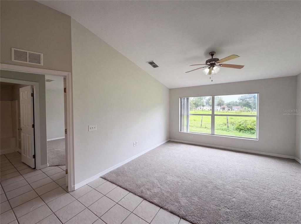 A room with beige carpet, a ceiling fan, and a view of a grassy field — 37209 GRASSY HILL LANE, DADE CITY, FL