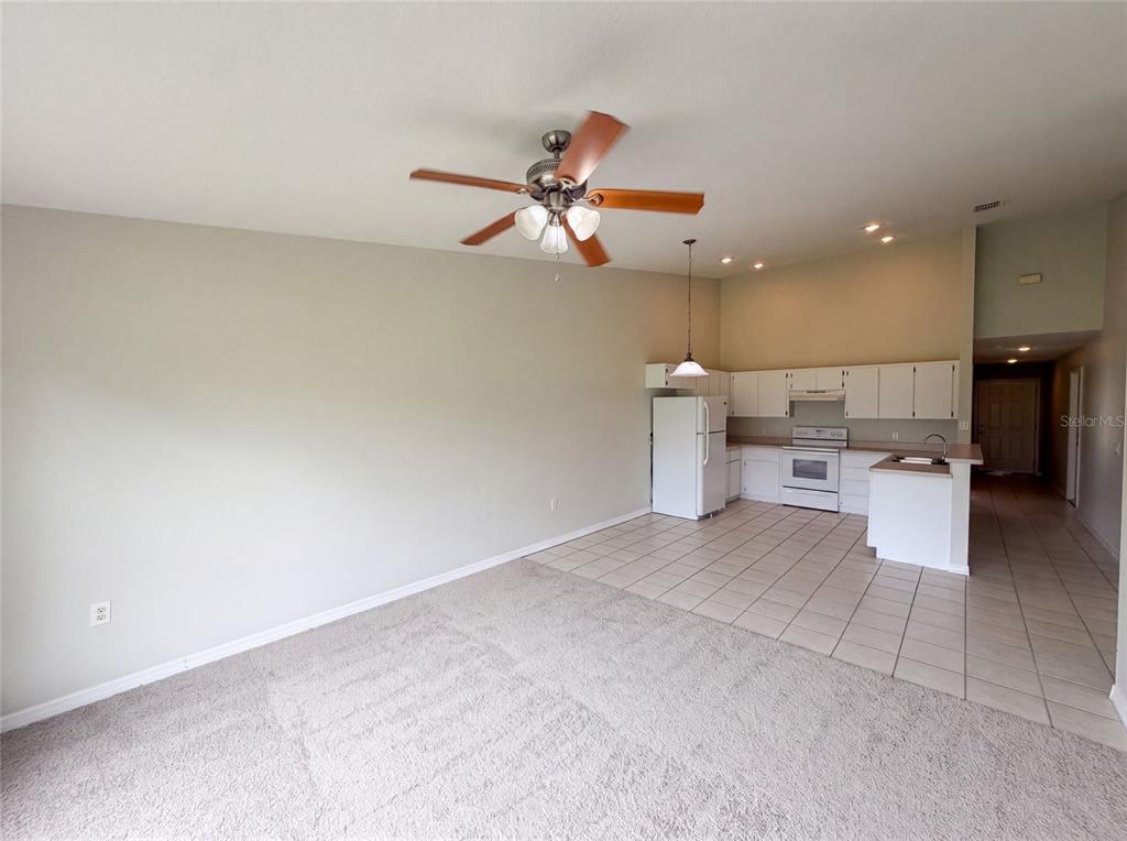 An open-concept room features a carpeted living area, a tiled kitchen, and a ceiling fan — 37209 GRASSY HILL LANE, DADE CITY, FL