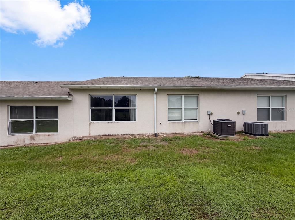 The exterior rear view of a single-story house shows four windows and two air conditioning units — 37209 GRASSY HILL LANE, DADE CITY, FL