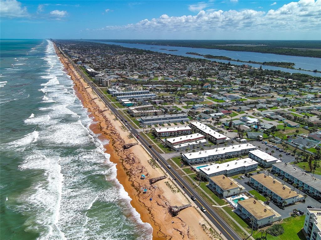 An aerial view shows a coastal town with multi-story buildings situated between the ocean and river — 2820 OCEAN SHORE BOULEVARD UNIT 150, ORMOND BEACH, FL