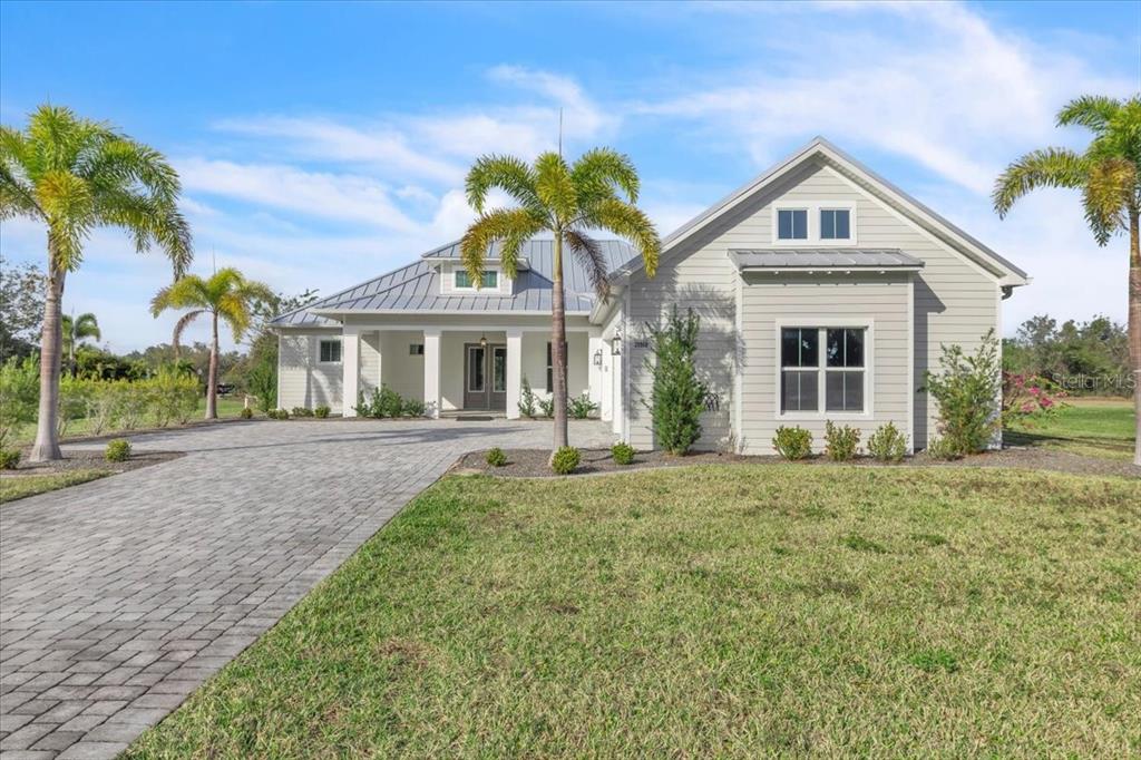 A light-colored, single-story house with a metal roof and a paved driveway features palm trees — 28960 GIN LANE, PUNTA GORDA, FL