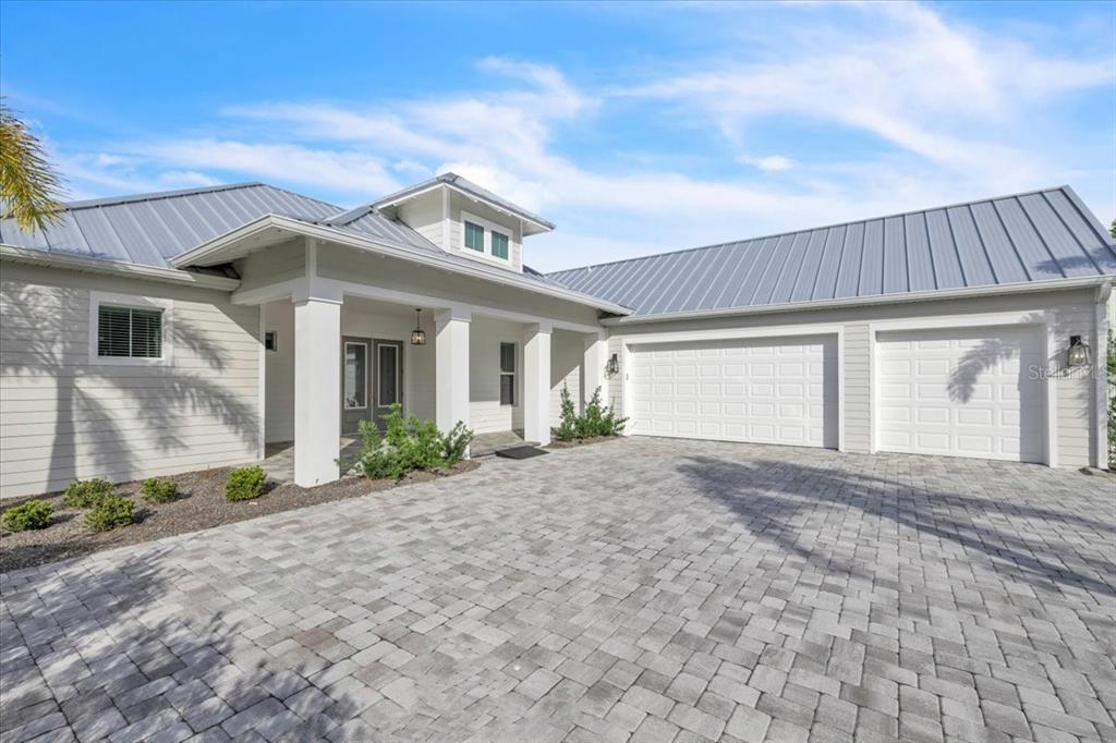 A light-colored house with a metal roof, a paver driveway, and a three-car garage — 28960 GIN LANE, PUNTA GORDA, FL
