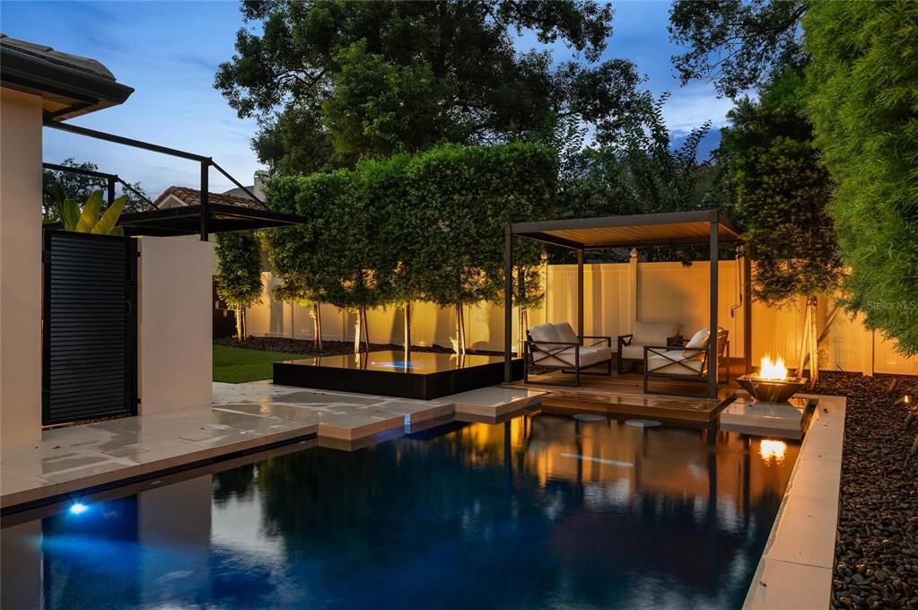 A backyard pool area features a modern pergola, lounge seating, and a fire pit at dusk — 7 W NEW HAMPSHIRE STREET, ORLANDO, FL